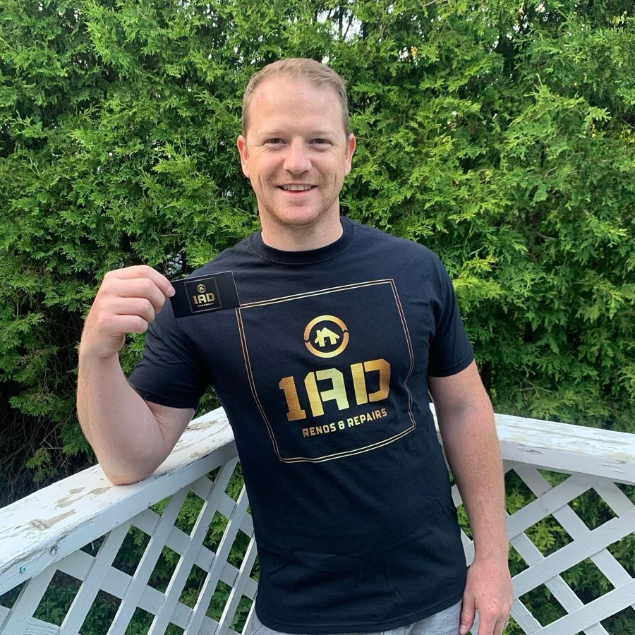The owner of 1AD Renovations in a 1AD shirt, holding a business card